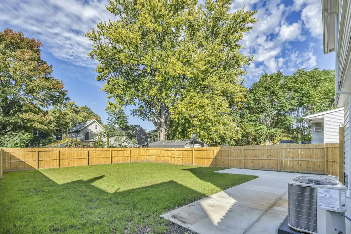 Fenced backyard with a central air conditioner condenser beside the patio