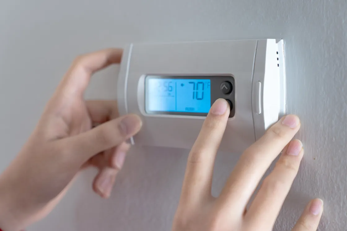 Hands adjusting a digital wall thermostat