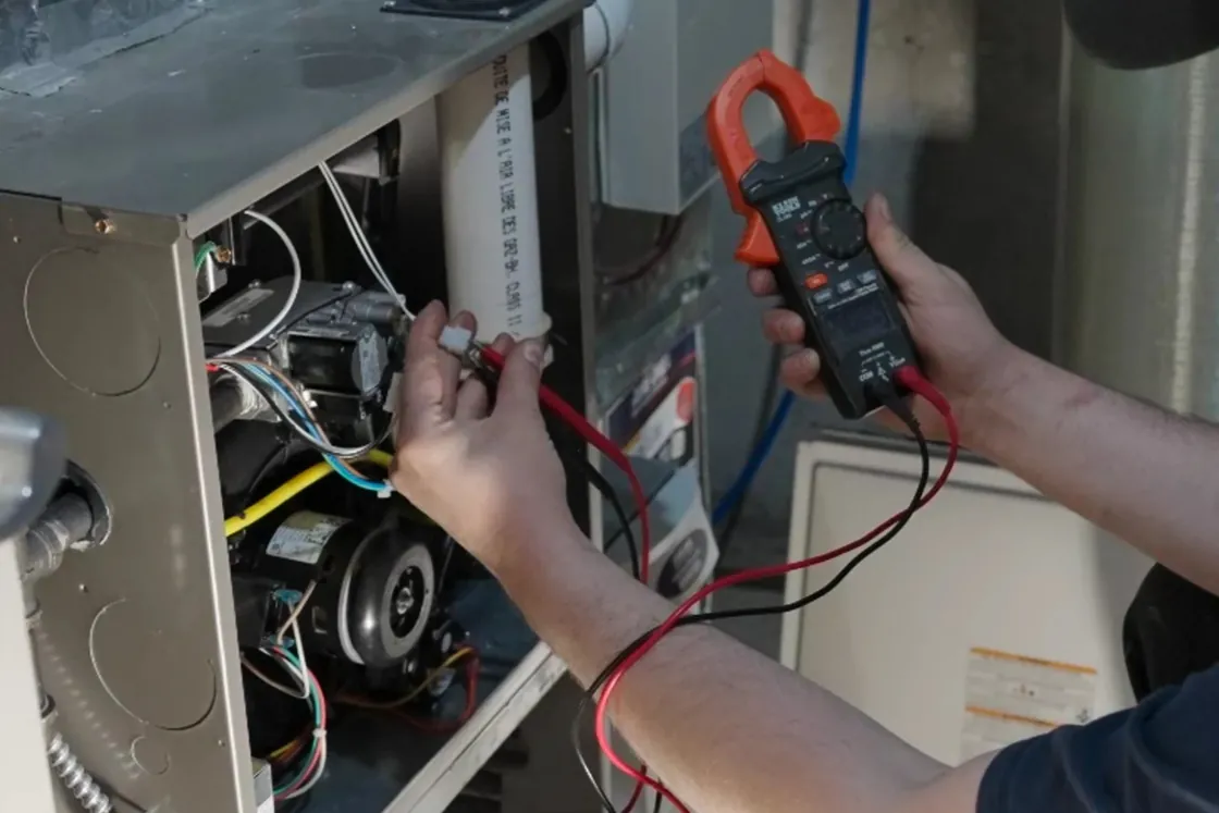 Technician testing furnace wiring with a clamp meter, front panel removed