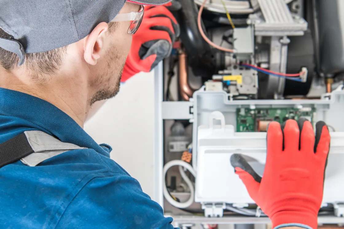Technician in work gloves checking the control board inside a heating unit