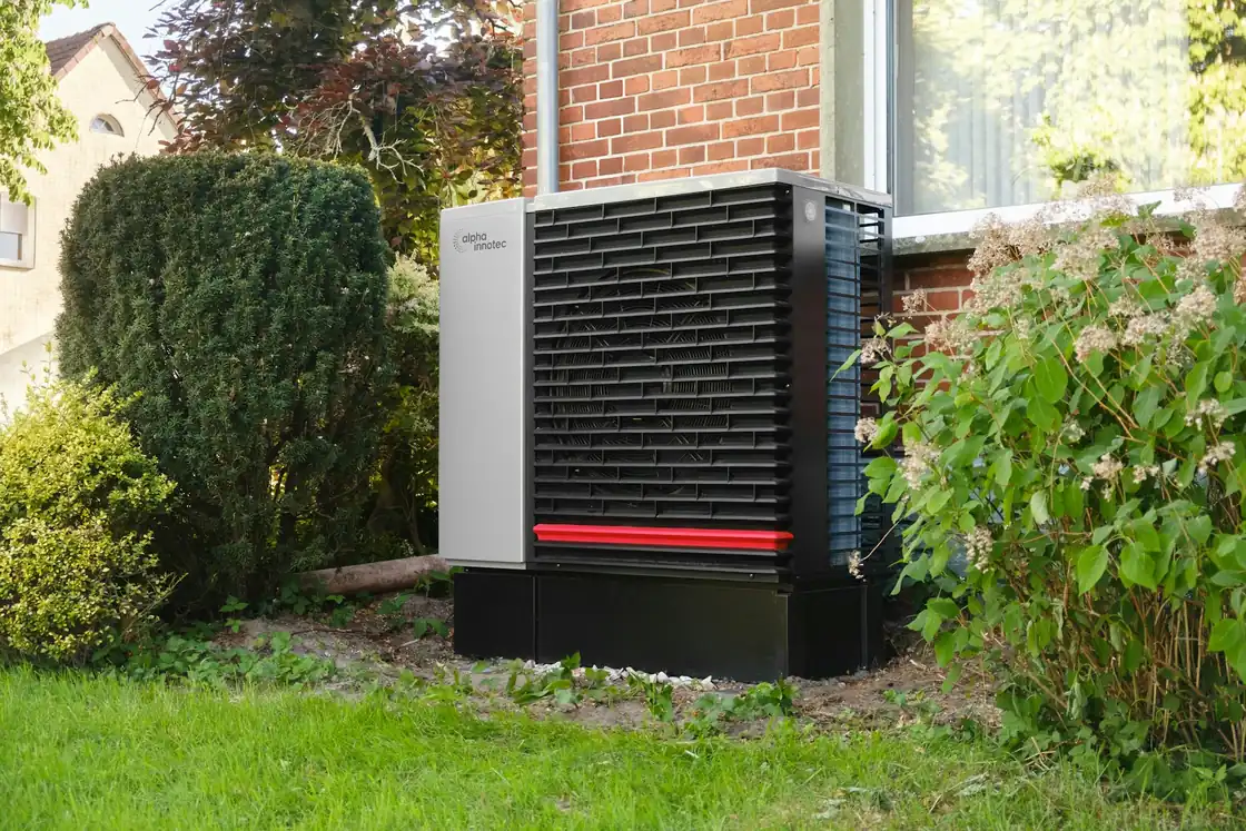 Outdoor heat pump unit beside a brick house in a garden