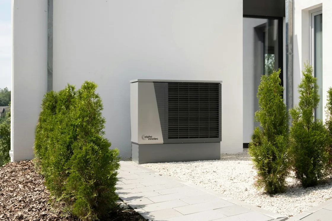 Outdoor heat pump unit on a gravel bed beside a modern white house