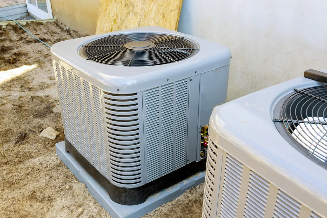 Two central air conditioner condensers on pads beside a house